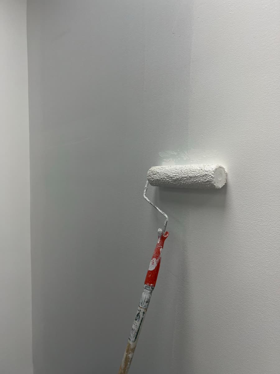 A roller laying a smooth coat of grey paint across an interior wall