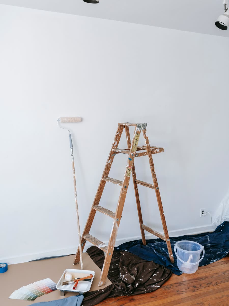 A paint-spattered wooden stepladder and roller against a freshly painted white wall